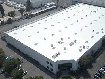 Arial view of white industrial building with white roof with aligned skylights and vents in rows