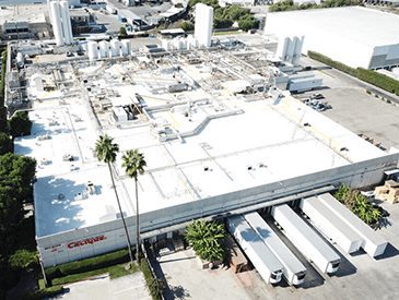 Arial view of Industrial building with a white roof with tractor trailers at loading docks