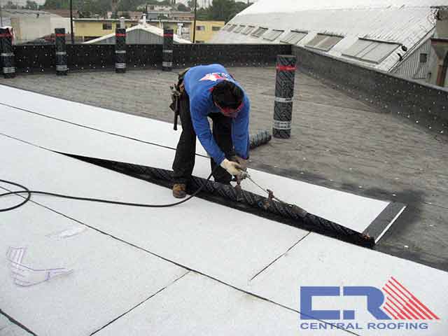 Man in blue shirt applying roofing material to freshly prepped industrial roof