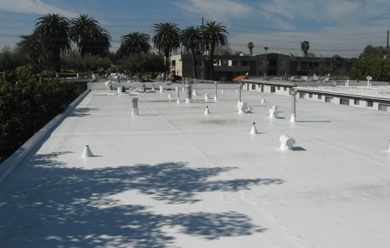 Flat white industrial roof with air vents on it with palm trees in the background