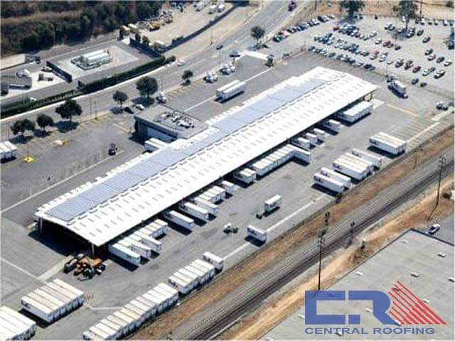 Arial view of long loading dock with white roof and many semi trailers backed in