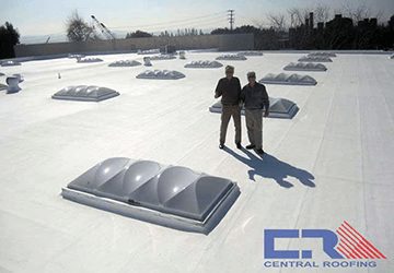 Two men standing on white industrial roof looking at a skylight
