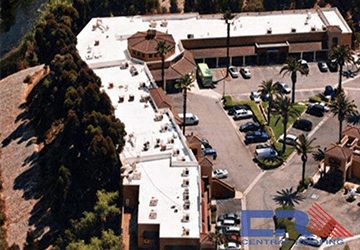 Arial view of L-shaped shopping center with white roof and cars in the parking lot