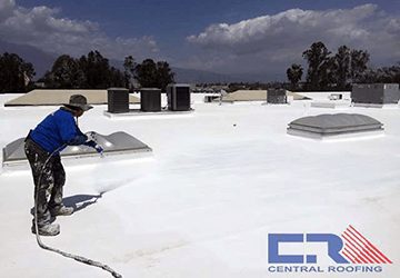 Man in blue shirt on top of white industrial roof with a hose spraying