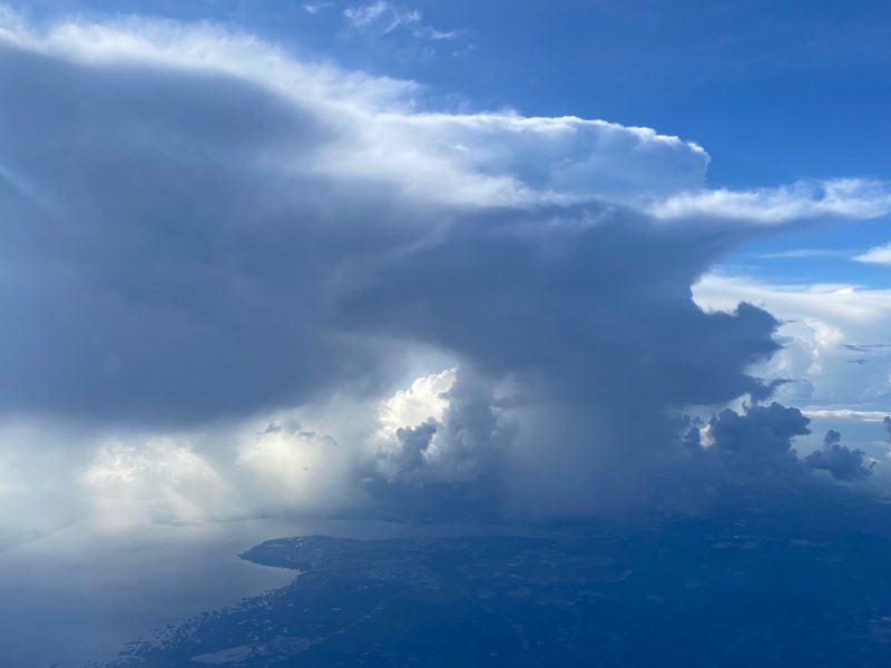 Arial view of storm clouds against blue skies with land and ocean below.